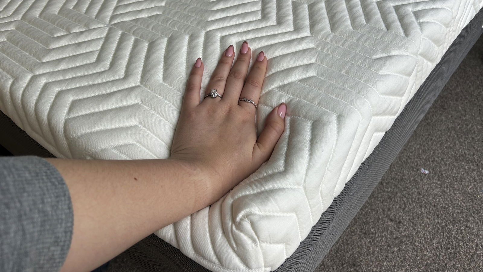 Hand with rings pushing down on the Valmori Hybrid II mattress corner with white and grey details