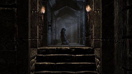 Skyrim console commands and cheats: A hooded figure kneels in the middle of a stone hallway, torches and moonlight providing the only source of light.